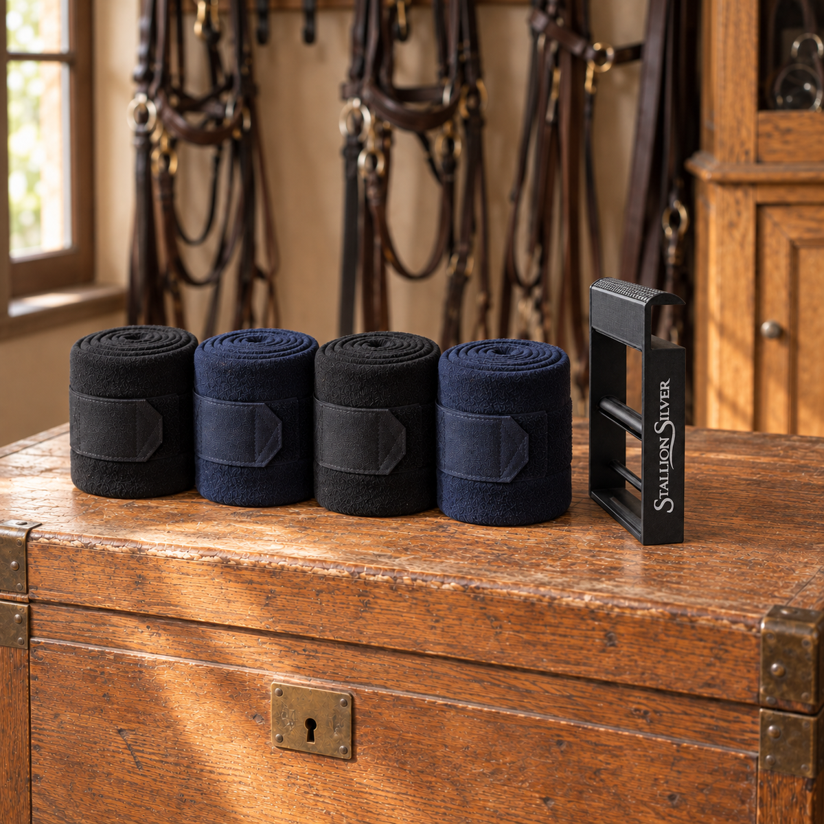 Four tightly rolled black and navy polo wraps lined up on a tack trunk lid beside the Stallion Silver wrap roller