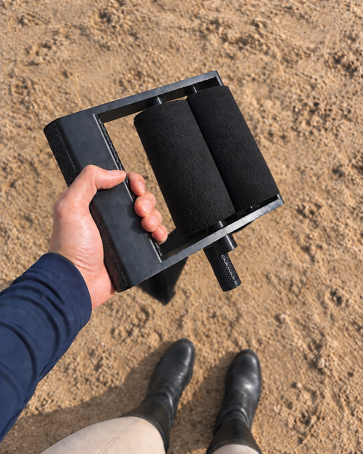 Rider's view of the black Stallion Silver wrap roller in hand with two rolled black wraps, sand arena below