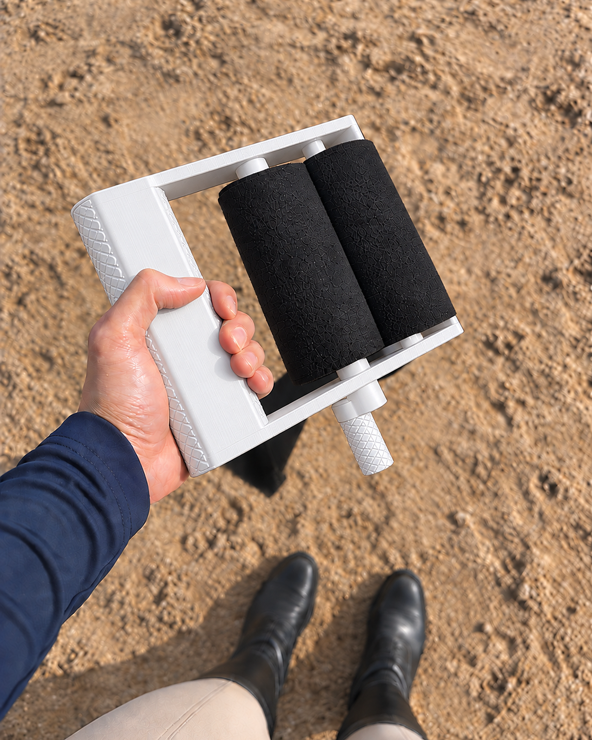 Rider's view of the white Stallion Silver wrap roller in hand with two rolled black wraps, sand arena below